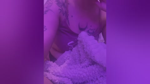 Media: Video of a woman with light skin, wearing a purple crop top, hugging a plush toy covered in white fur. She has multiple tattoos on her arms and chest, partially visible. The background is a gradient of purple hues, creating a soft, intimate atmosphere.