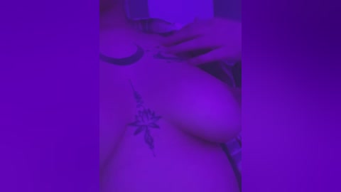 Media: Video of a nude, fair-skinned person with a visible tattoo of a small, intricate flower on their lower abdomen, set against a purple backdrop, creating a soft, ethereal ambiance.