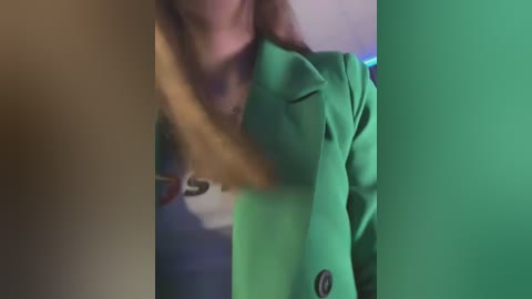 Media: Video of a woman in a bright green jacket, blurred in the foreground, with a green screen background, suggesting a green screen studio setting.