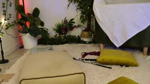 Media: Video of a cozy, dimly lit room with a beige pouf, a yellow cushion, and a green chair, adorned with greenery and fairy lights, creating a serene, festive atmosphere.