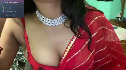 Media: Video of a woman with light skin, wearing a red saree with gold trim and a diamond choker, holding a phone displaying a Lovense app.