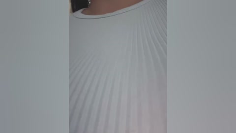 Media: Video of a woman's torso wearing a ribbed, long-sleeved, white cotton top with a round neckline. The image is focused on the upper body, emphasizing the textured fabric.