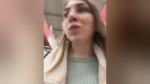 Media: Video of a young Caucasian woman with fair skin and light brown hair, wearing a light blue top, looking upwards with a neutral expression. Background includes a red and white striped balloon and a beige jacket.