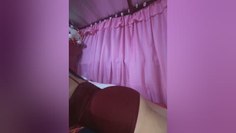 Media: A video of a cozy bedroom with pink curtains, a red blanket, and a brown pillow on a beige bed, under a wooden ceiling. The room has a warm, inviting ambiance.