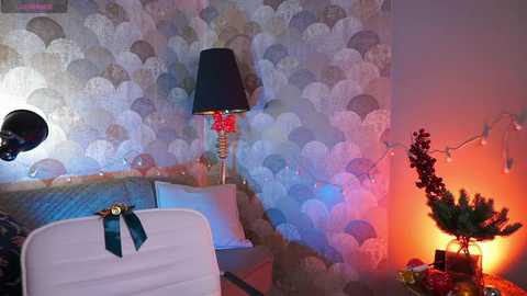 Video of a cozy, festive room with a bed adorned with a white blanket and teal ribbon, a patterned wallpaper, a black lamp, a small Christmas tree, and warm, ambient lighting.