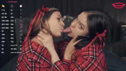 Media: Video of two young women in red plaid shirts, kissing each other's tongues, in a dimly lit bedroom with a video chat interface on the left.