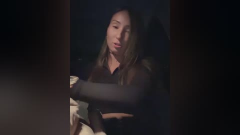 Media: A dimly lit video shows an Asian woman with long, straight hair, wearing a black top, seated on a bed, eyes closed, in a contemplative pose.