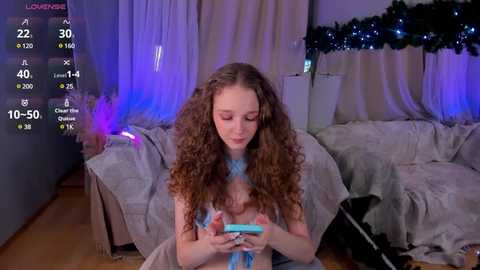 Media: A video of a young woman with curly brown hair, wearing a blue top, sitting on a sofa in a cozy, dimly lit room with Christmas decorations, playing a Nintendo Switch.