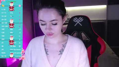 Media: Video of a young woman with light skin, dark hair, and a white robe, sitting in a gaming chair. Overlayed with a colorful, animated chart.