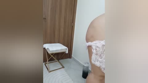 Media: Video of a partially visible woman in white lace lingerie, standing in a minimalist bathroom with wooden door, white walls, and a towel rack.