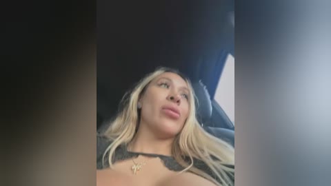 Media: Video of a blonde woman with a fair complexion, wearing a black top, leaning back in a car, looking upward with a pouty expression.