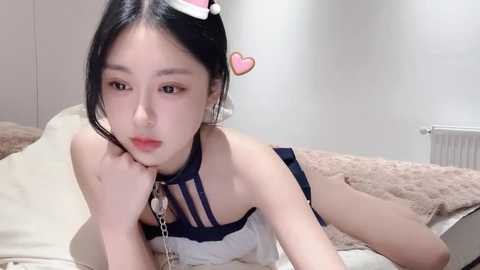 Media: Video of an East Asian woman with long black hair, wearing a black and white lingerie set, lying on a bed in a minimalist room with beige walls.