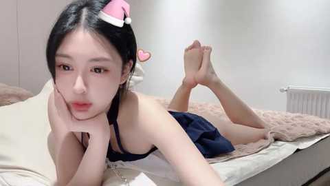 Media: A video of an East Asian woman with fair skin, black hair, and a pink hat, lying on a bed in a white room, wearing a black bikini.