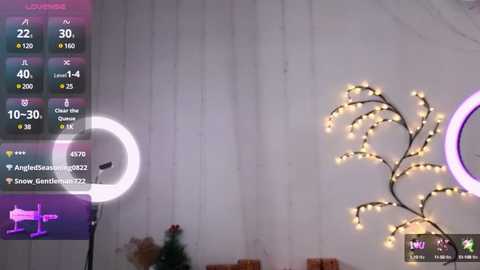 Media: Video of a dimly lit room featuring a large, glowing, multi-colored ring light on the left, a white wall, and a decorative, string-lit tree on the right.