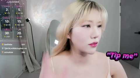 Media: A video of a young Asian woman with blonde hair, wearing a pink dress, sitting indoors. The image is overlaid with a digital display showing \"Tip me\" and social media handles.