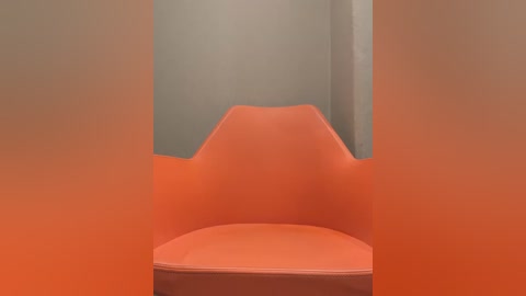 Media: A video showcasing an orange, curved-back chair with a smooth, matte finish, set against a plain beige wall. The chair's design is modern and minimalist, with a slight curve at the backrest.