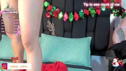 Media: Video of a person in a teal bikini standing next to a bed with a black headboard, adorned with red and green tinsel and a decorative feather.