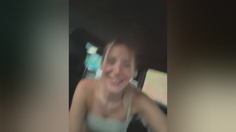 Media: A blurred video shows a smiling woman with blonde hair in a car, wearing a strapless top. The background is dark, with indistinct shapes and light sources.