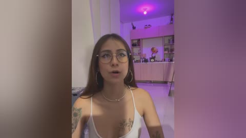 Media: A video of a young woman with long brown hair, wearing glasses, a white camisole, and hoop earrings, standing indoors with a bookshelf in the background, illuminated by purple lighting.