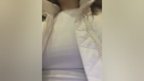 Media: A video of a person wearing a white puffy jacket and a white shirt, with blurred facial features and arms partially visible, creating a soft focus effect.