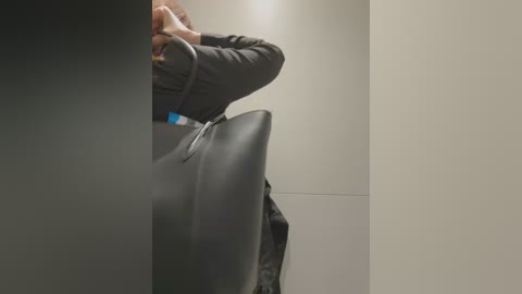 Media: A video showing a person in a dark jacket, holding a large black handbag, standing in a dimly lit, minimalist hallway with beige walls. The person's face is partially obscured by the bag.