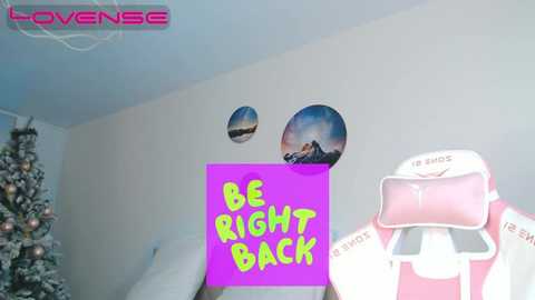 Media: Video of a modern room with a pink gaming headset and a purple sign reading \"BE RIGHT BACK\" on a white wall, featuring a framed landscape and a decorated Christmas tree in the background.