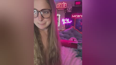 Media: Video of a young woman with long blonde hair, wearing glasses, smiling, standing in a neon-lit room with a purple bed and a \"MIRAN\" sign.