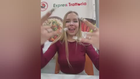 Media: Video of a blonde woman in a red top, smiling and holding up a pizza, surrounded by colorful fast-food advertisements in a restaurant.