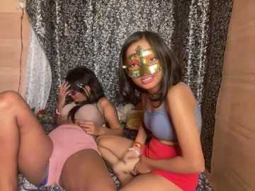 Media: Video of three women with dark skin, one wearing a gold mask, lying on a bed with patterned sheets, wearing pink and red lingerie.