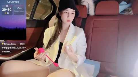 Media: Video of an Asian woman with long hair, wearing a black beanie, white jacket, and shorts, using a pink vibrator inside a car.