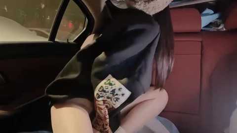 Media: Video of a woman with long brown hair in a black dress, holding a small, patterned handbag, sitting in a red car, with a blurred background.