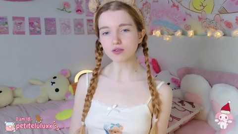 Media: A video of a young, fair-skinned woman with long, blonde braided pigtails, wearing a white tank top and cat ears, in a whimsical, pink-themed room filled with plush toys and fairy lights.