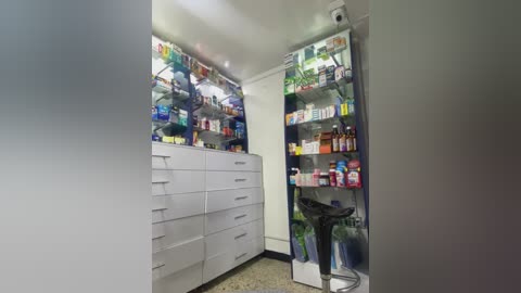 Media: Video of a well-lit, organized medicine cabinet with white shelves and drawers, displaying various pharmaceutical items and a stool.