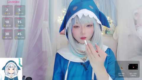 Media: Video of a pale-skinned, anime-inspired cosplay girl with blue hair, donning a blue shark costume and holding a lollipop. Background features soft pastel curtains and a \"Live\" overlay with stats.