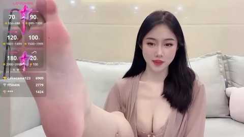 Media: A video of an East Asian woman with long black hair, wearing a pink robe, lying on a white couch, displaying a virtual foot size of 70 in a digital overlay.