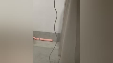 Media: Video of a pink, cylindrical sex toy lying on a gray concrete floor, near a white wall with a black electrical outlet. The room is dimly lit, creating a somber, minimalist ambiance.