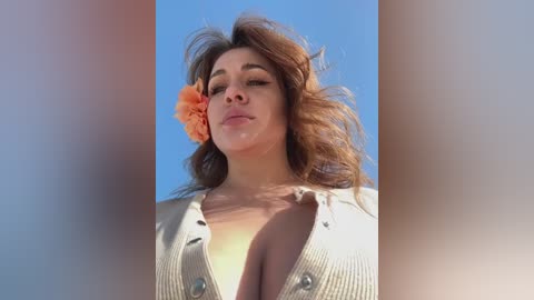 Media: Video of a young woman with light brown hair, large breasts, and a flower in her hair, wearing a low-cut white shirt, against a bright blue sky.