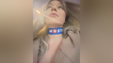 Video of a blonde woman with fair skin, wearing a blue \"MST\" collar necklace, captured from a low angle, with a slight lens flare.