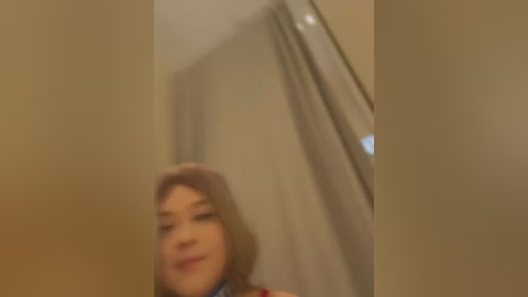 Media: A blurry video of a woman with light skin, possibly of Asian descent, wearing a red dress and a pink headband, standing in front of a beige curtain.