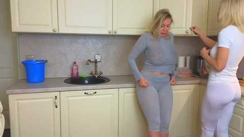 Media: Video of two women in matching grey athletic wear, one with a ponytail, in a modern, beige kitchen with cabinets, sink, and countertop.