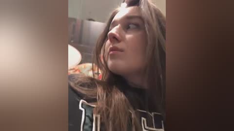 Media: A video of a young woman with long, light brown hair, wearing a black and white shirt, gazing thoughtfully into the distance. Background includes blurred furniture and a warm, ambient lighting.