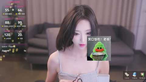 Media: A video of an Asian woman with straight black hair, wearing a gray camisole, sitting in a modern living room. Virtual avatars, including a green frog, overlay the image.