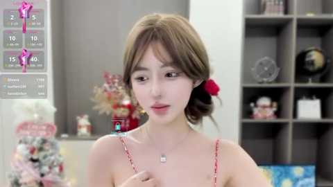 Media: Video of an Asian woman with light skin and brown hair, wearing a red spaghetti-strap top, standing in a modern, minimalist room with grey shelves and Christmas decorations.