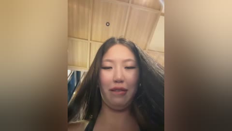 Media: Video of a young Asian woman with long, straight black hair, light skin, and closed eyes, standing in a wooden-paneled room.