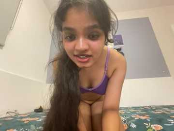 Media: Video of a young woman with long dark hair, wearing a purple bra, leaning forward in a bedroom with a blue-patterned bedspread.