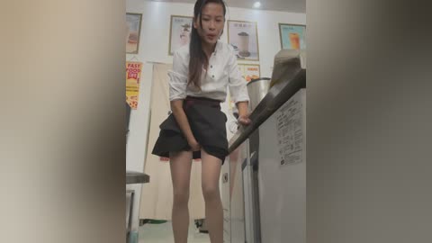 Media: Video of an Asian woman in a white blouse and black skirt, working at a coffee machine in a dimly lit cafe, with posters of drinks on the wall.