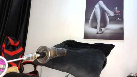 Media: Video of a modern, minimalist room featuring a black leather chair with a red and black bag on the left. A large painting of a nude woman in a pose holding a wine glass hangs on the white wall.