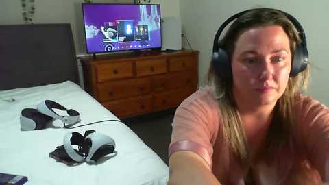 Media: A video of a woman wearing black headphones, sitting on a bed, with a TV displaying a game console interface in the background.