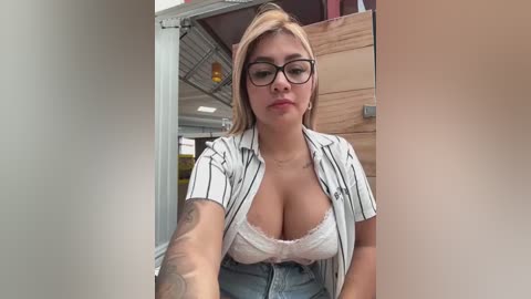 Media: Video of a plus-sized woman with fair skin, blonde hair, wearing glasses, a white striped shirt, and a lacy white bra, leaning against a wooden structure, with a tattoo on her right arm.