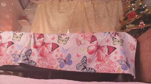 Media: Video of a bedspread with a whimsical pink and white pattern featuring butterflies and flowers. The bed is against a wall adorned with fairy lights and a small Christmas tree on the right.